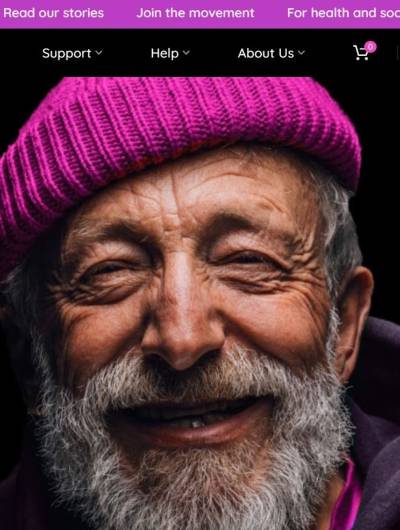 A close-up headshot of a smiling man with a white beard and a magenta-pink beanie fills the frame. The top of the image features a website's navigation bar, partially obscured, with links related to stories and community engagement.